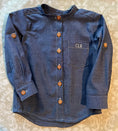 Load image into Gallery viewer, a flat view of the blue chambray button down shirt showing the detail of the pocket monogram in the same contrasting white thread