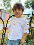 Load image into Gallery viewer, Little boy outside a gate wearing a white linen button down shirt with a poet color, natural wood buttons and monogram pocket