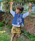 Load image into Gallery viewer, Little boy wearing the off white linen button back shirt, textured chambray vest in blue and pleated cuffed shorts in khaki