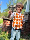 Load image into Gallery viewer, Little boy wearing our organic corduroy vest printed with large oranges and buttons down the front with wood buttons. He's also wearing our off white linen button down shirt and textured skinny jeans