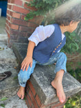 Load image into Gallery viewer, Little boy wearing distressed skinny jeans, textured blue chambray vest with close wood buttons down the front and white linen shirt with buttons down the back