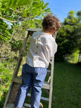 Load image into Gallery viewer, Little boy on a ladder with a back view of the off white linen shirt showing the natural wood buttons down the back