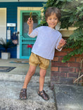 Load image into Gallery viewer, Little boy wearing an off white linen shirt with raglan sleeves and khaki colored pleated shorts with a cuffed hem
