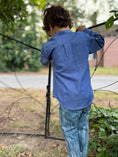 Load image into Gallery viewer, another picture of the back of the blue chambray button down shirt showing the pleat detail and curved hem
