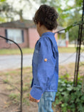 Load image into Gallery viewer, a side view of the blue chambray button down showing the wood button on the outside of the sleeve for the sleeve tab when rolled up and buttoned
