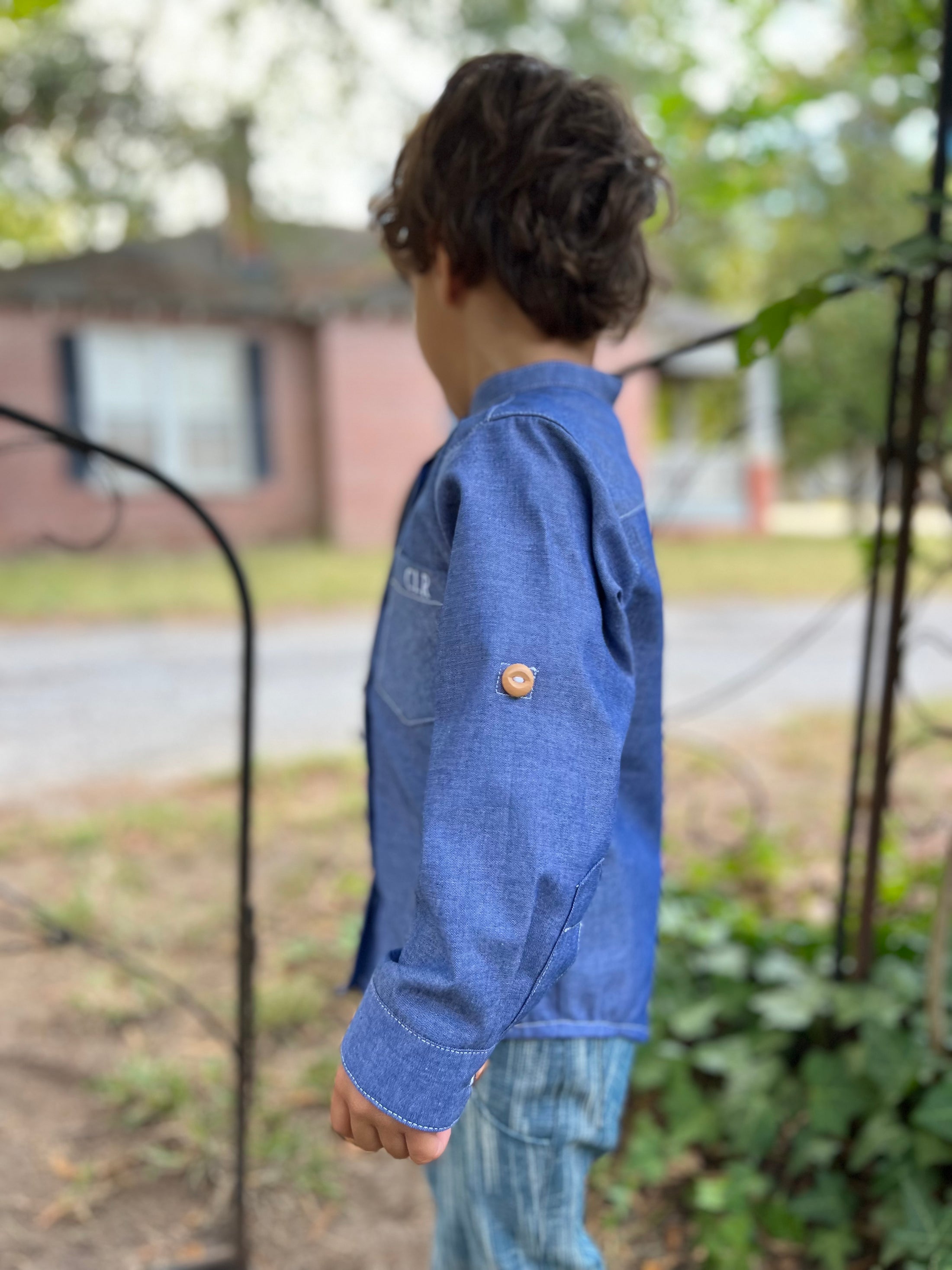 a side view of the blue chambray button down showing the wood button on the outside of the sleeve for the sleeve tab when rolled up and buttoned