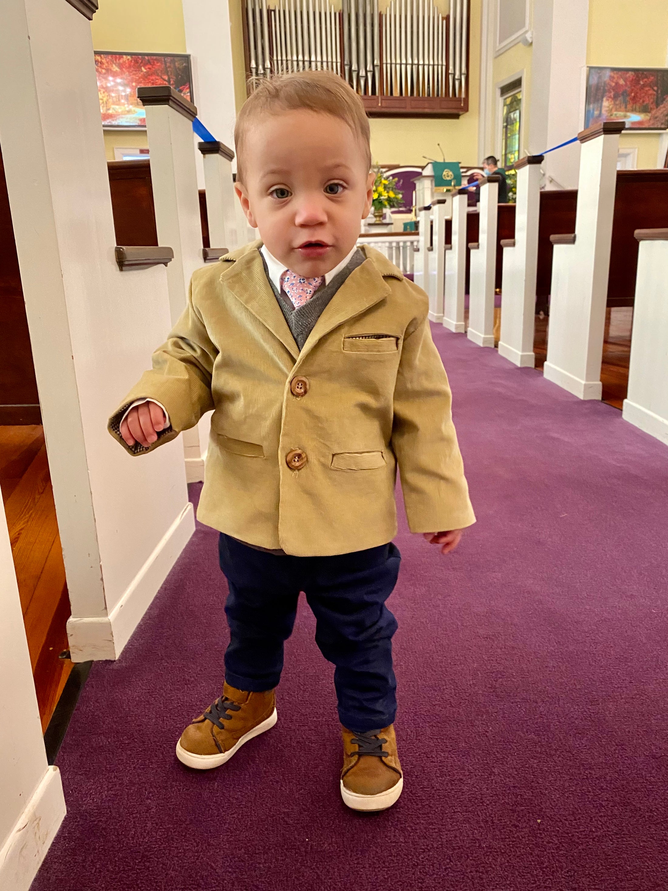 toddler boy standing in a church with a tan corduroy sportscoat with wood buttons