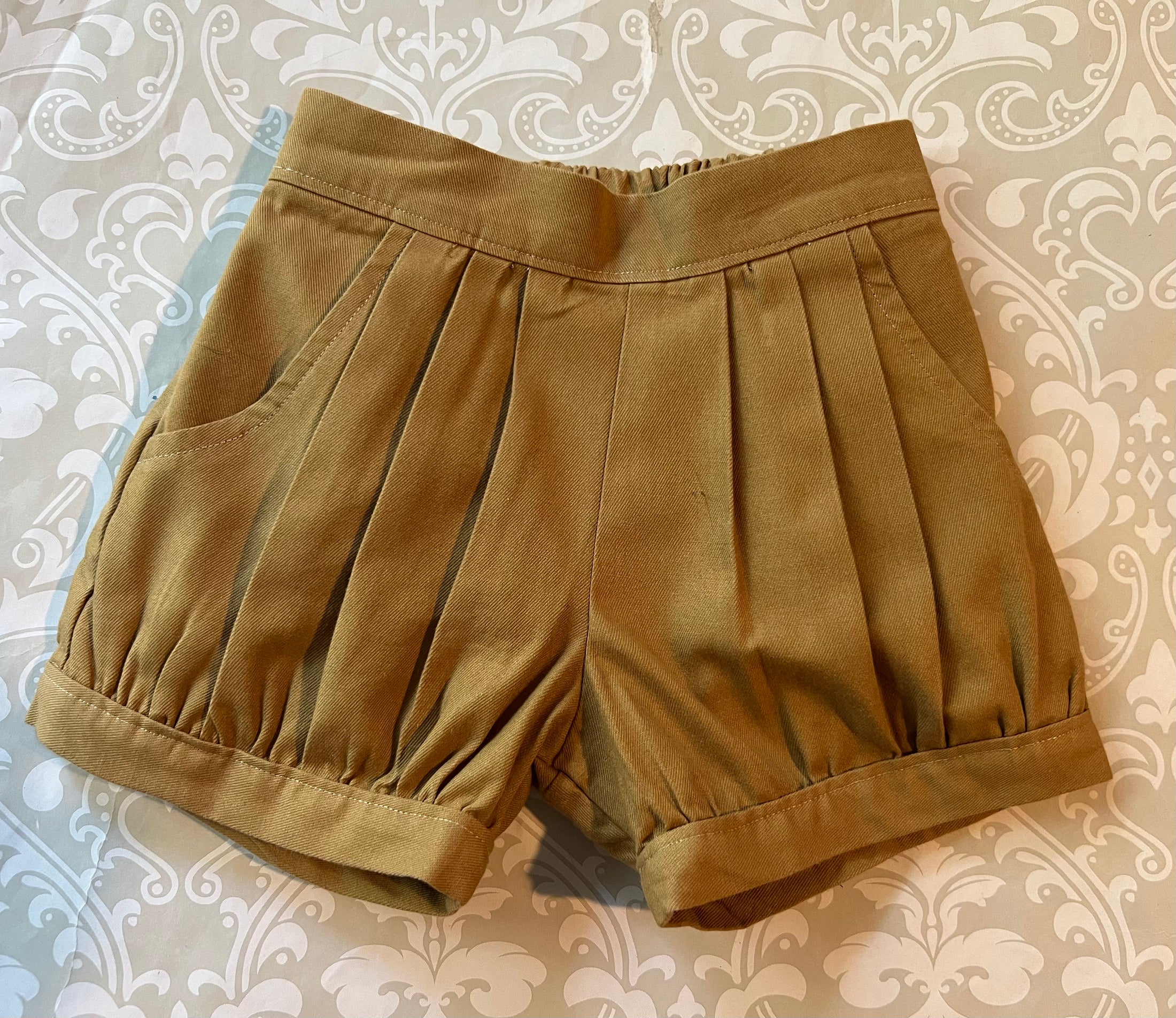 flat lay view of the pleated cuffed shorts showing the topstitch detail on the flat front waistband and cuffs at the legs