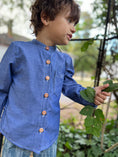 Load image into Gallery viewer, Little boy wearing a blue chambray long sleeve button down shirt with poet collar and wood buttons
