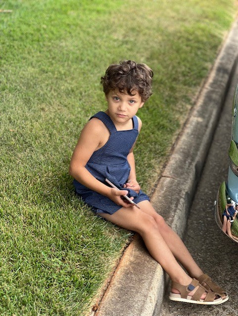 Little boy sitting on a curb wearing the vintage style romper