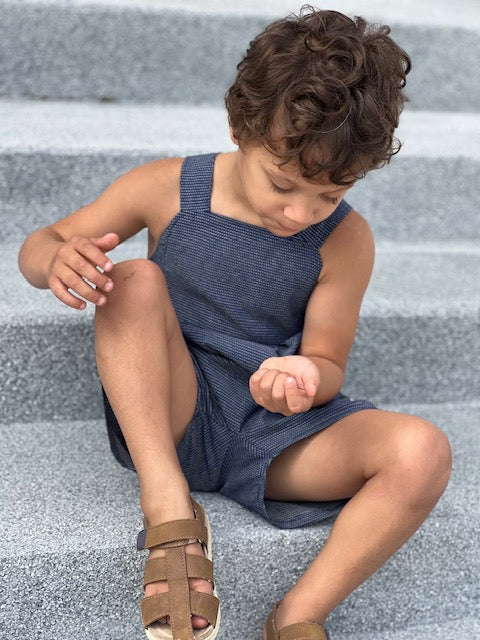little boy sitting on steps showing the front bib detail and pleats of the romper
