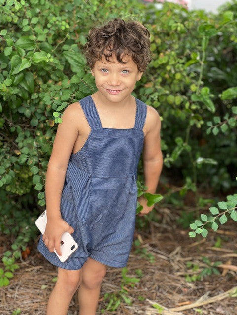 little boy standing outside showing the full detail of the vintage style romper with the pleats on the mid sides just under the bodice