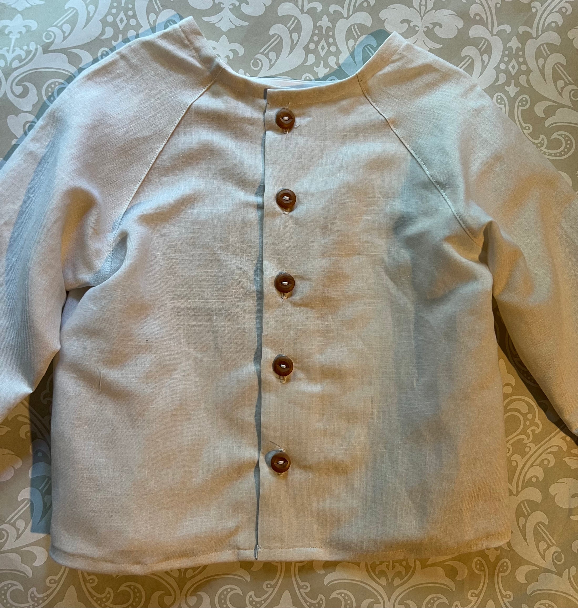 Flat view of the off white linen button back shirt showing the topstitch detail and natural wood buttons down the back