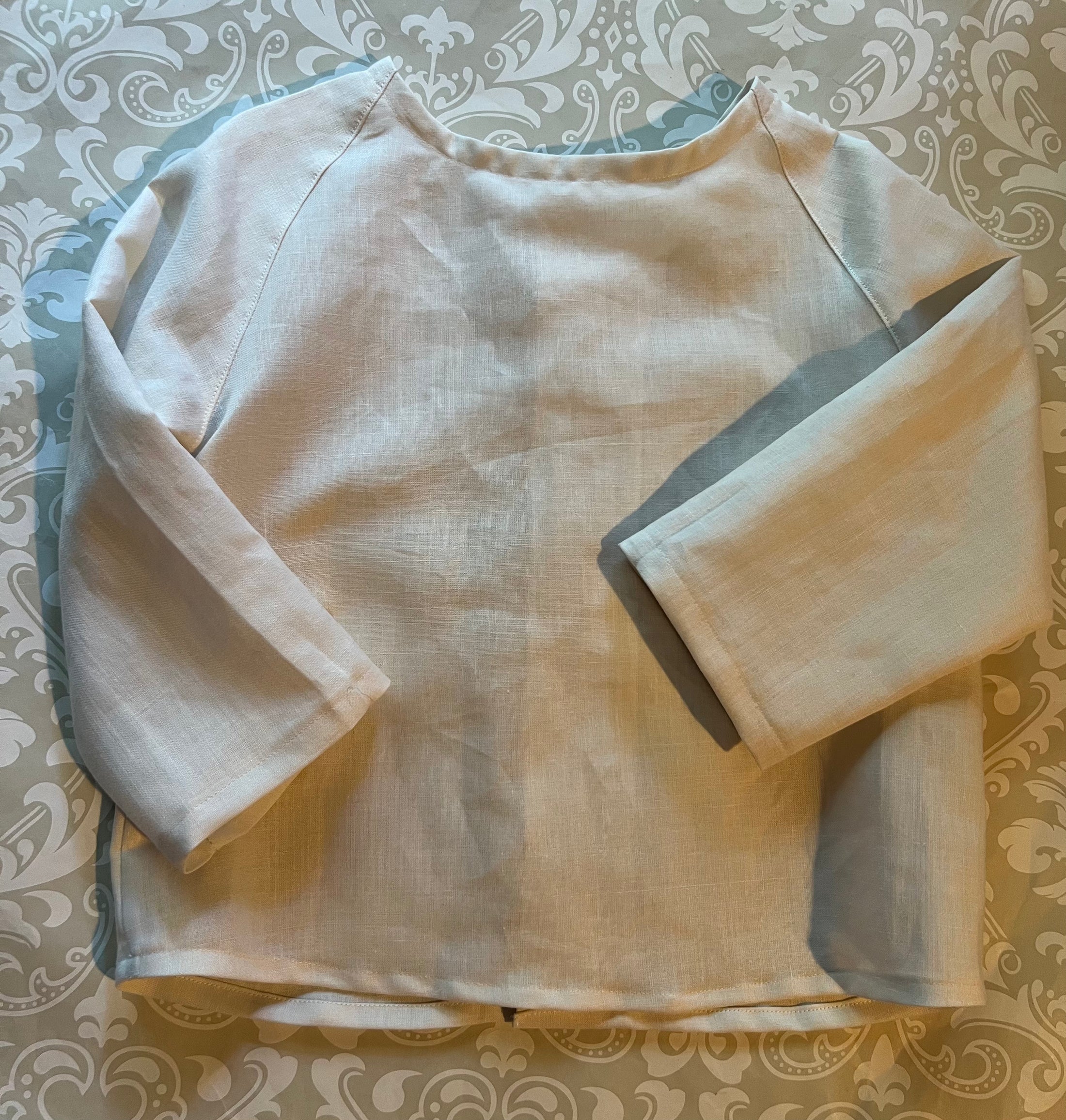 flat view of off white linen shirt showing the top stitch detail of the raglan sleeves