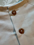 Load image into Gallery viewer, Closeup view of the natural wood 2 hole buttons on the off white linen button back shirt
